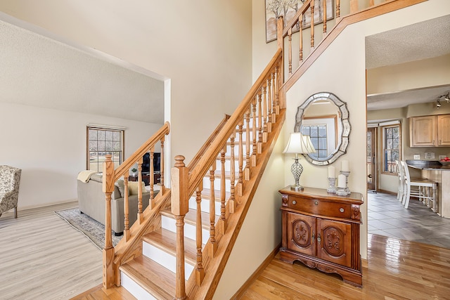 staircase featuring a textured ceiling, baseboards, wood finished floors, and a healthy amount of sunlight