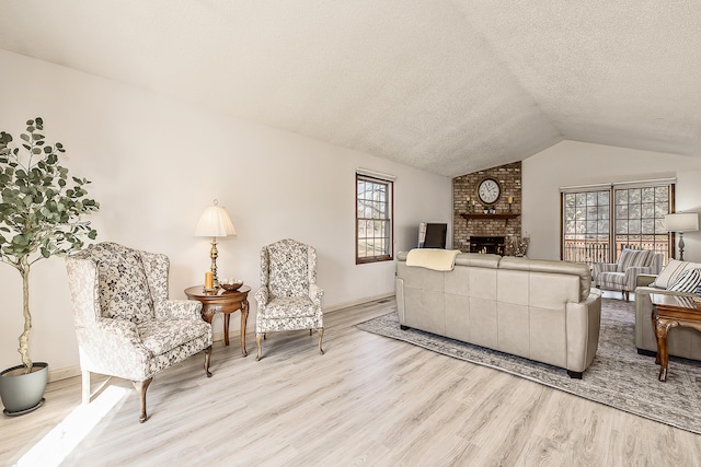 living room with lofted ceiling, a textured ceiling, a fireplace, baseboards, and light wood-style floors