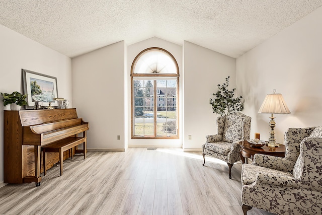 sitting room featuring light wood-type flooring, vaulted ceiling, a textured ceiling, and baseboards