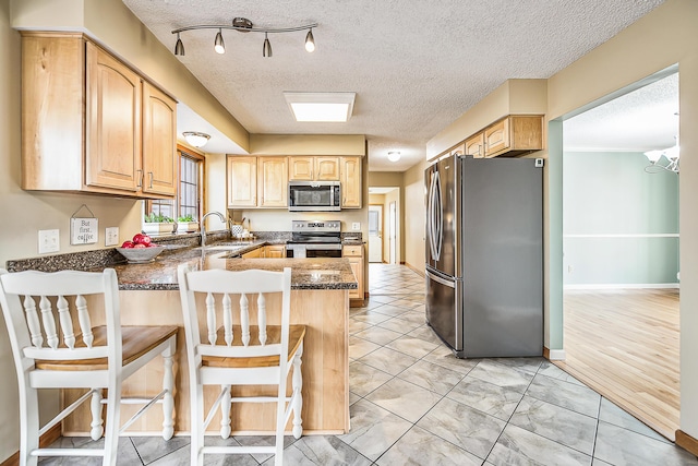 kitchen featuring appliances with stainless steel finishes, light brown cabinets, a sink, a peninsula, and a kitchen bar