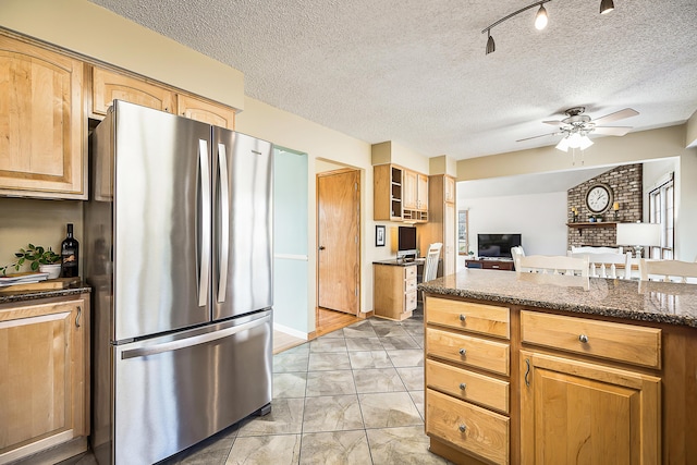 kitchen featuring dark stone counters, ceiling fan, glass insert cabinets, freestanding refrigerator, and a textured ceiling