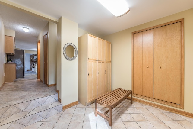 hall featuring light tile patterned floors, baseboards, and a textured ceiling