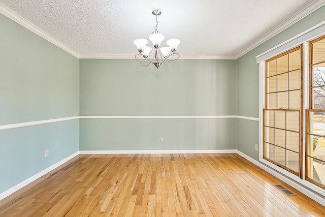 empty room featuring visible vents, hardwood / wood-style floors, an inviting chandelier, ornamental molding, and baseboards