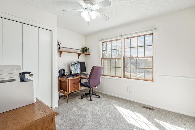 office space featuring a textured ceiling, light colored carpet, a ceiling fan, baseboards, and visible vents