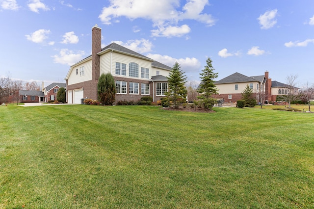 rear view of house featuring a garage, brick siding, a lawn, and a chimney