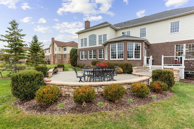 back of house with a yard, a patio area, a chimney, and brick siding