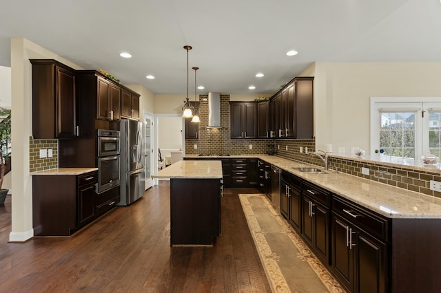 kitchen with stainless steel appliances, a sink, dark brown cabinets, dark wood-style floors, and wall chimney exhaust hood