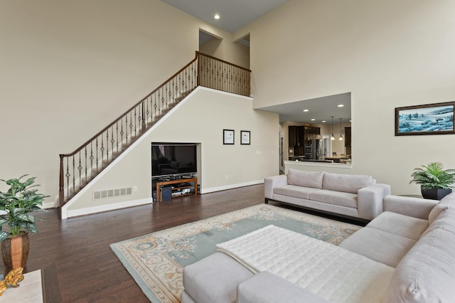 living room with baseboards, visible vents, a towering ceiling, wood finished floors, and stairs