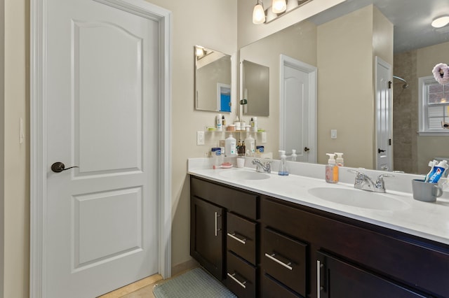 bathroom with a tile shower, double vanity, and a sink