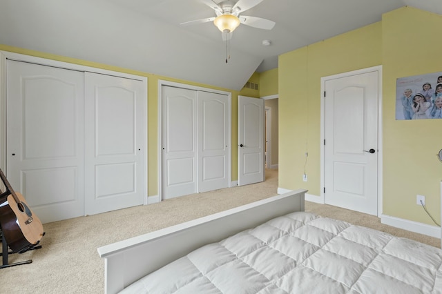 bedroom with baseboards, light colored carpet, ceiling fan, vaulted ceiling, and multiple closets