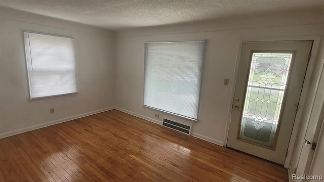 interior space with baseboards, visible vents, hardwood / wood-style flooring, a textured ceiling, and a wealth of natural light