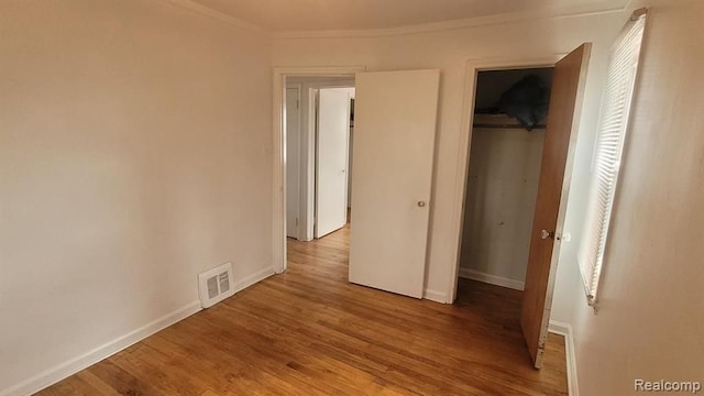 unfurnished bedroom with visible vents, baseboards, light wood-style floors, ornamental molding, and a closet