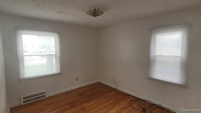 spare room with a healthy amount of sunlight, a textured ceiling, visible vents, and wood finished floors