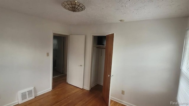 unfurnished bedroom featuring baseboards, visible vents, wood finished floors, a textured ceiling, and a closet