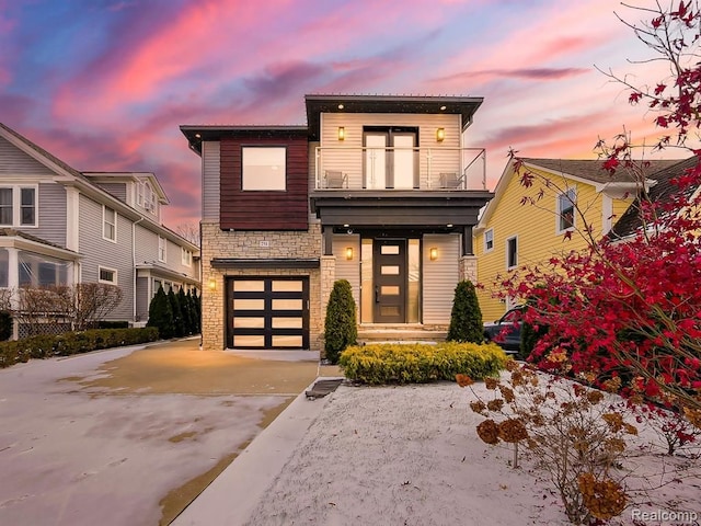 modern home with a balcony, stone siding, driveway, and an attached garage