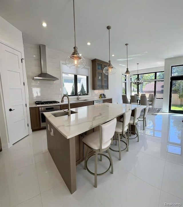 kitchen featuring a kitchen island with sink, a sink, backsplash, wall chimney exhaust hood, and stainless steel gas stovetop