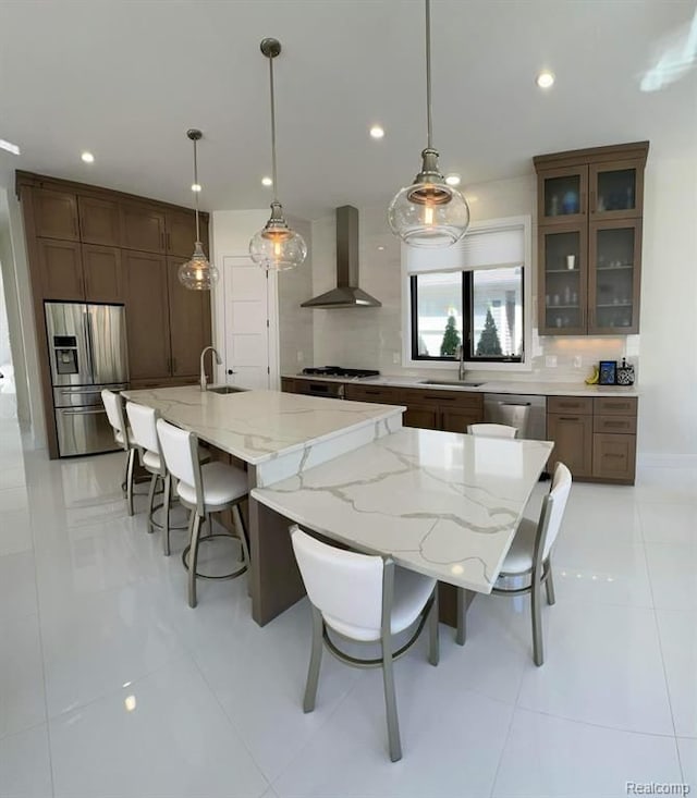 kitchen featuring stainless steel appliances, tasteful backsplash, a sink, wall chimney range hood, and a kitchen breakfast bar