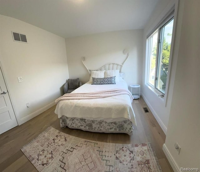 bedroom with baseboards, visible vents, and wood finished floors