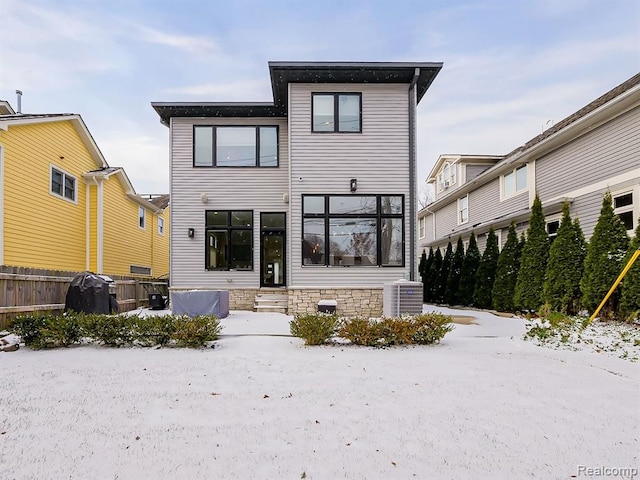 snow covered back of property featuring entry steps, central AC, and fence