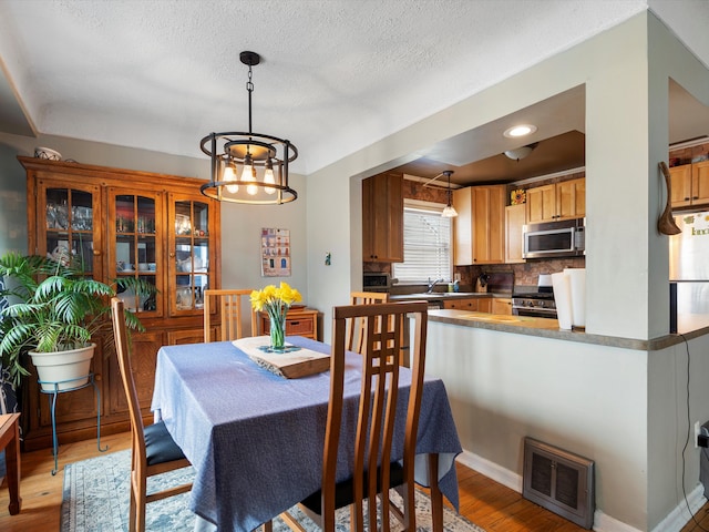 dining area with visible vents, a textured ceiling, light wood-style flooring, and baseboards