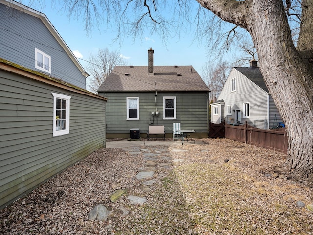 back of property with roof with shingles, a chimney, a patio area, central AC, and fence