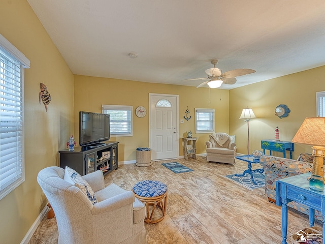 living room featuring ceiling fan, baseboards, and a wealth of natural light