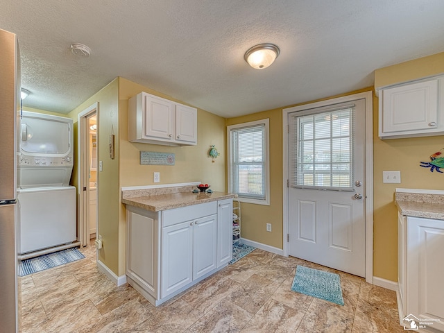 kitchen featuring light countertops, stacked washer / dryer, white cabinetry, a textured ceiling, and baseboards