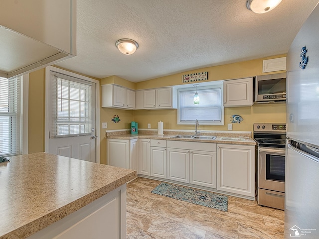 kitchen featuring stainless steel appliances, a textured ceiling, light countertops, white cabinetry, and a sink