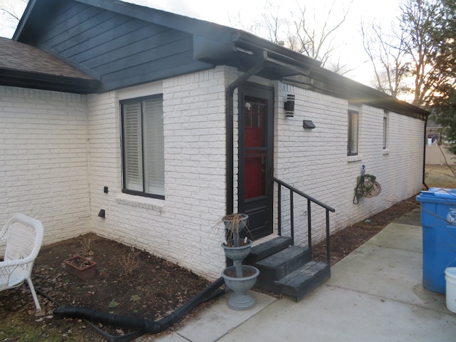 doorway to property with brick siding and roof with shingles