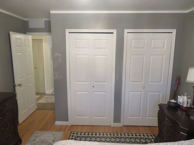 bedroom featuring crown molding, light wood finished floors, baseboards, and two closets