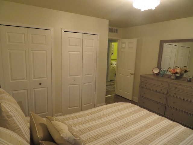 bedroom featuring dark wood finished floors, baseboards, visible vents, and two closets