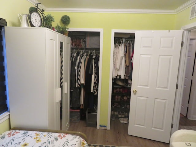 bedroom featuring wood finished floors, two closets, visible vents, and ornamental molding