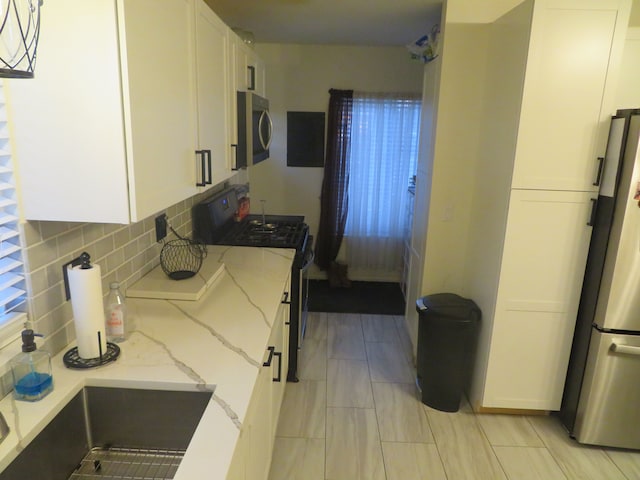 kitchen with light stone counters, decorative backsplash, white cabinets, and appliances with stainless steel finishes