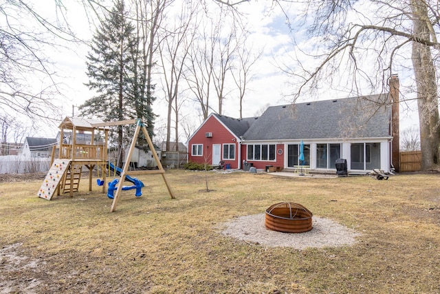 rear view of property with a playground, a yard, a chimney, fence, and a fire pit