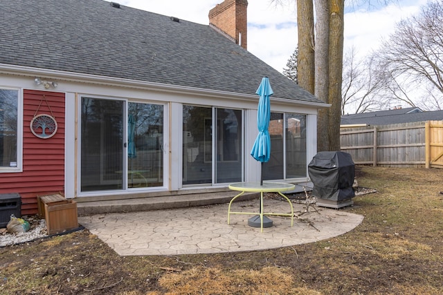 rear view of house with a shingled roof, fence, a chimney, and a patio