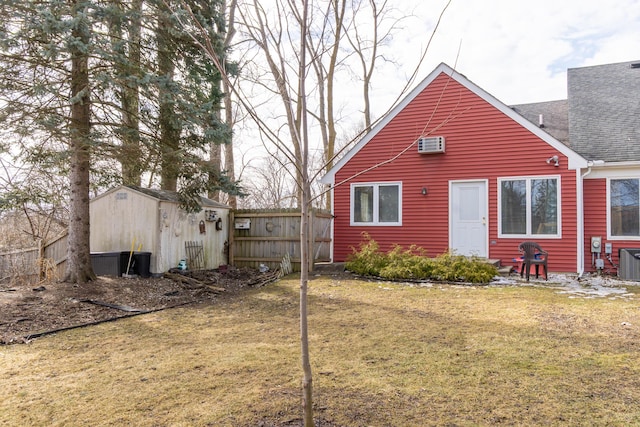 rear view of house featuring a shingled roof, a lawn, a wall mounted air conditioner, an outdoor structure, and central air condition unit