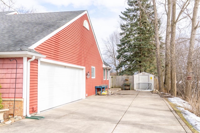 view of home's exterior with a garage, a storage unit, roof with shingles, and fence