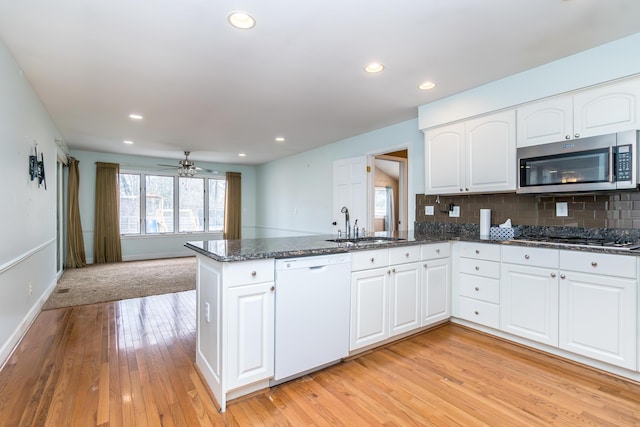 kitchen with dishwasher, stainless steel microwave, dark stone countertops, a peninsula, and a sink