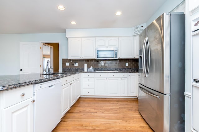 kitchen featuring stainless steel appliances, decorative backsplash, white cabinets, dark stone countertops, and light wood-type flooring