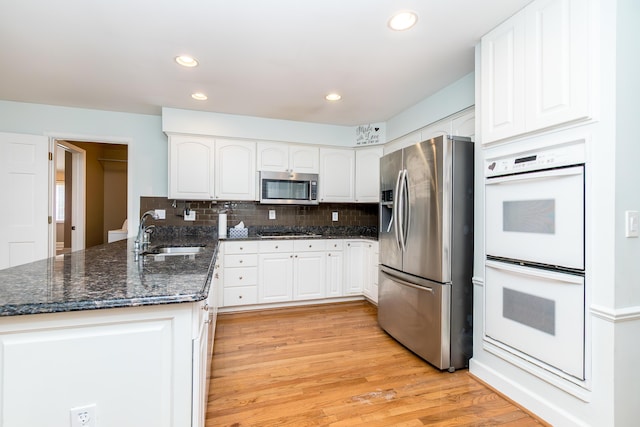 kitchen featuring stainless steel appliances, a peninsula, a sink, and white cabinetry