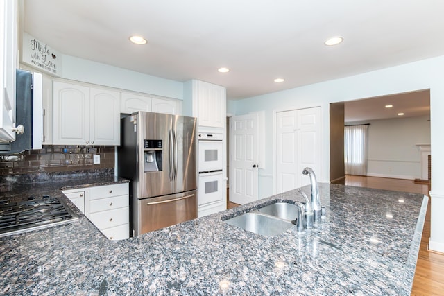 kitchen featuring appliances with stainless steel finishes, light wood-style floors, white cabinetry, a sink, and dark stone counters