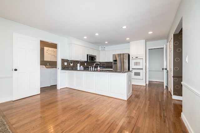 kitchen with a peninsula, appliances with stainless steel finishes, independent washer and dryer, and white cabinets