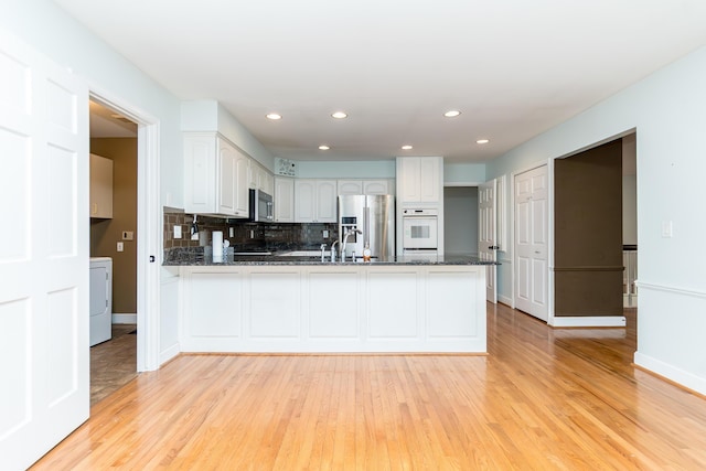 kitchen featuring washer / dryer, white cabinets, light wood-style flooring, appliances with stainless steel finishes, and a peninsula