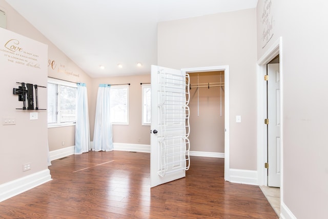 empty room featuring visible vents, vaulted ceiling, baseboards, and wood finished floors