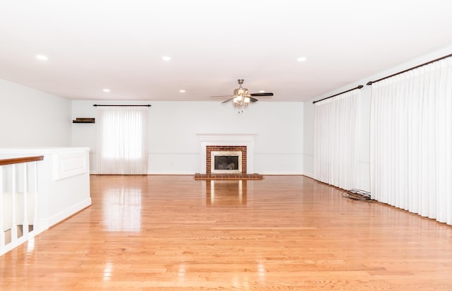 unfurnished living room with baseboards, light wood-style floors, ceiling fan, a brick fireplace, and recessed lighting