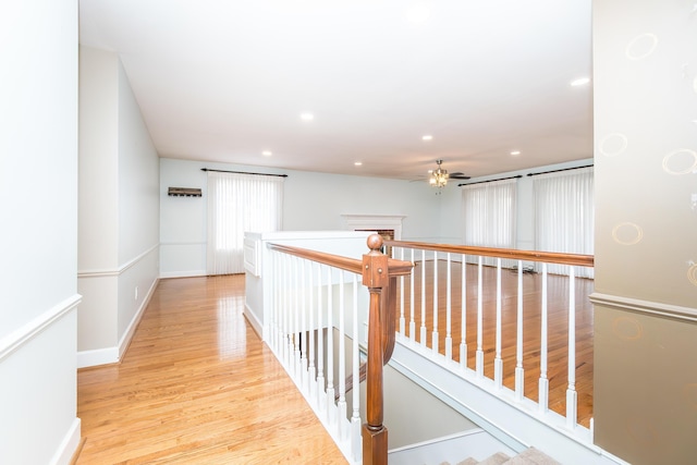 hallway featuring baseboards, light wood-type flooring, an upstairs landing, and recessed lighting