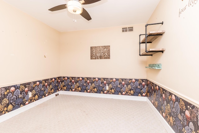 spare room featuring a wainscoted wall, a ceiling fan, baseboards, visible vents, and wallpapered walls