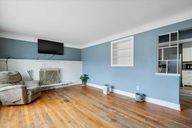 unfurnished living room featuring built in features, a brick fireplace, baseboards, and wood finished floors