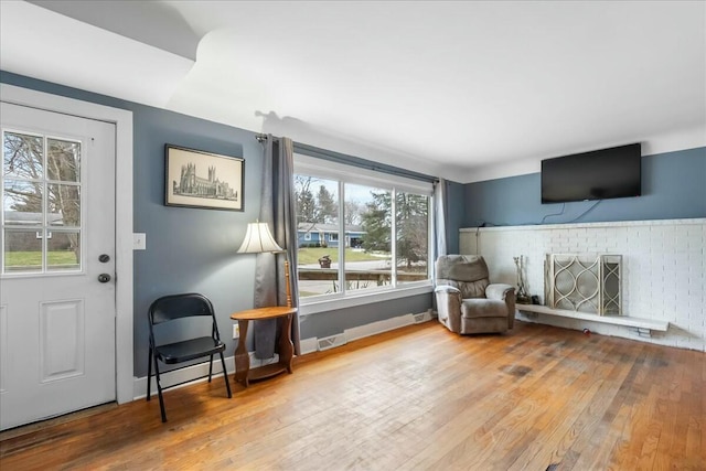 sitting room featuring a brick fireplace, baseboards, and wood finished floors