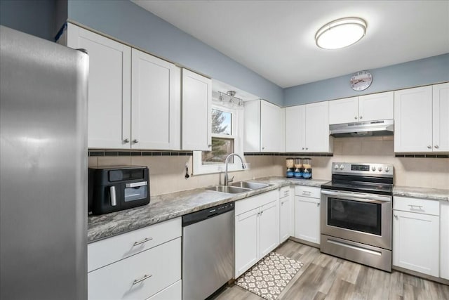 kitchen with light wood finished floors, appliances with stainless steel finishes, white cabinets, a sink, and under cabinet range hood